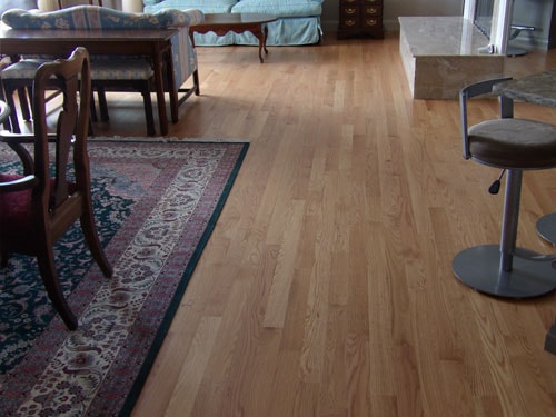 Warm natural oak hardwood floor in open-plan living and dining room with Persian area rug and bar stools