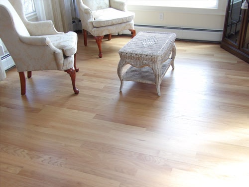 Bright living room with natural oak hardwood floor, white wing chairs, and wicker coffee table