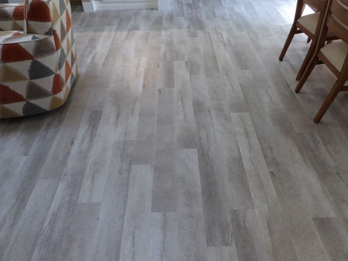Driftwood gray LVP luxury vinyl plank floor in living room with geometric-print sofa and wood chairs