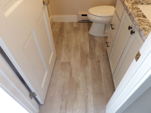 Light wood-look LVP flooring in small bathroom with white vanity, granite countertop, and white panel door