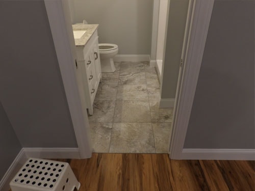 Gray stone-look tile floor in half bath viewed through doorway with hardwood floor transition in foreground
