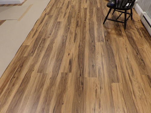 Warm pecan-tone LVP luxury vinyl plank flooring installation in progress in empty room with black chair
