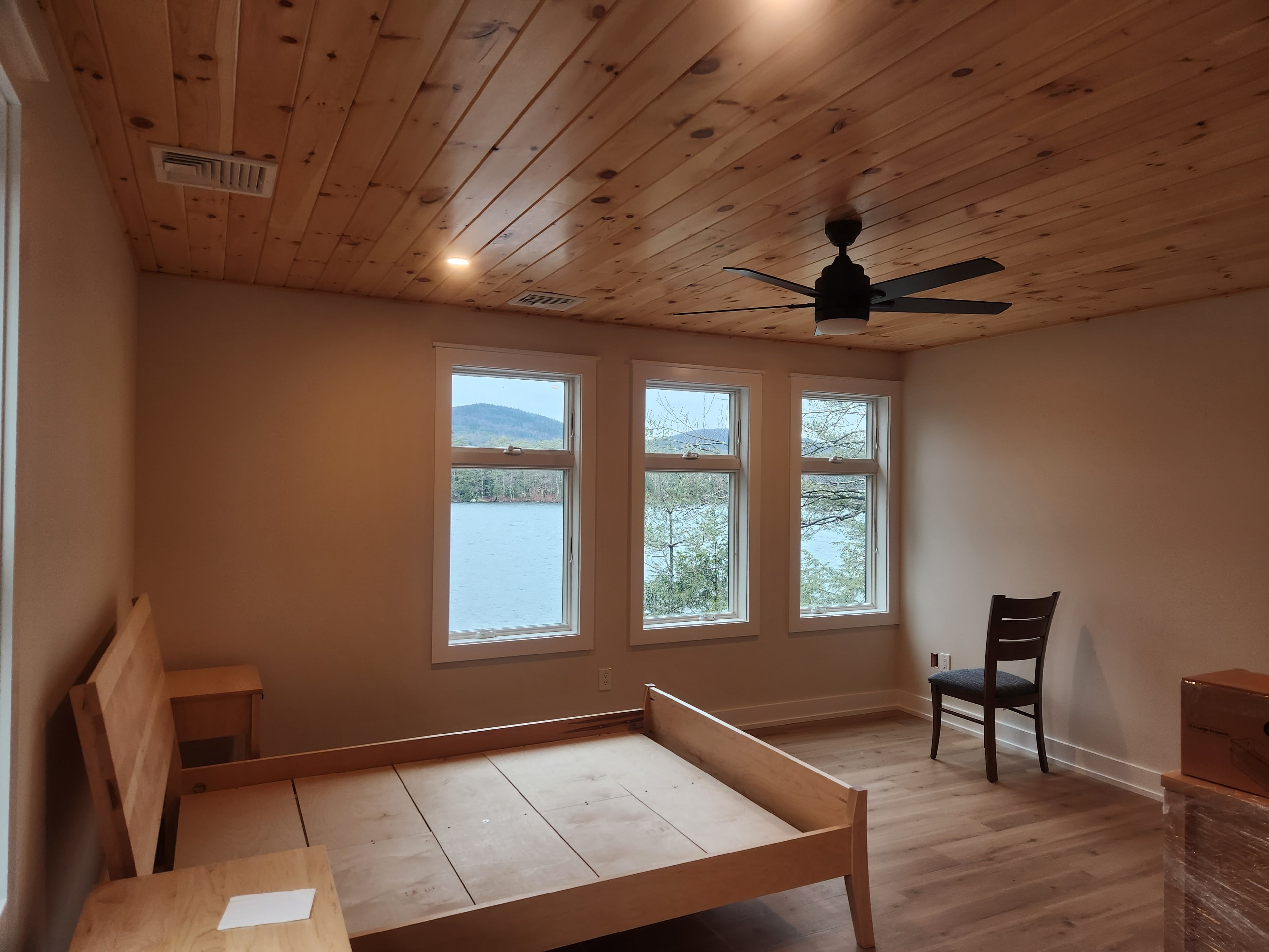 Finished lakeside master bedroom with knotty pine ceiling, lake views through triple windows, and hardwood floor