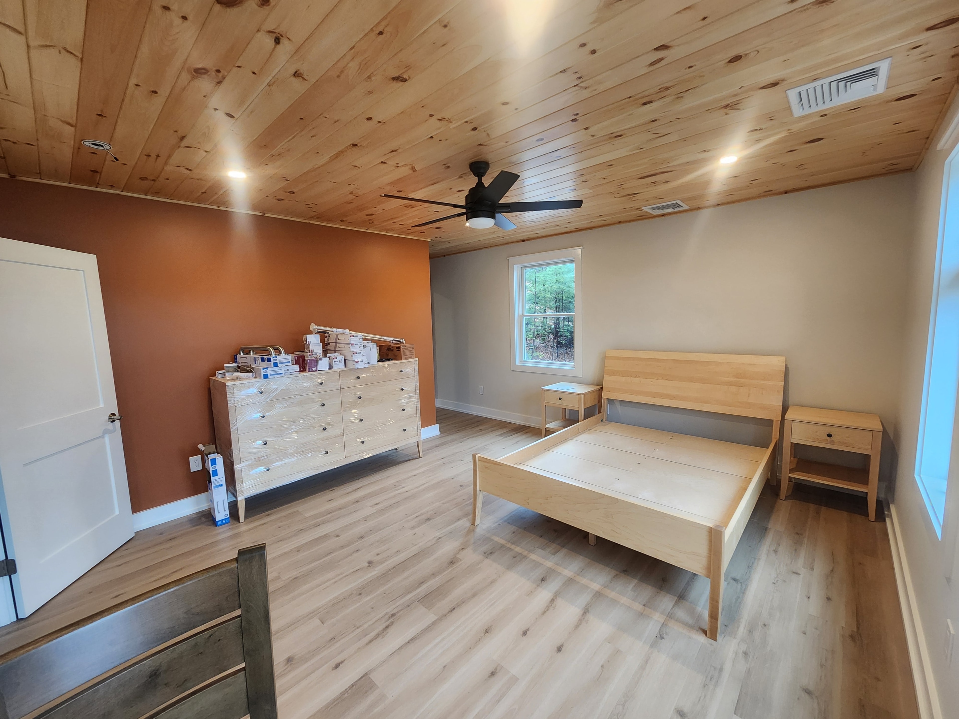 Finished bedroom with knotty pine ceiling, orange accent wall, maple furniture, and LVP flooring