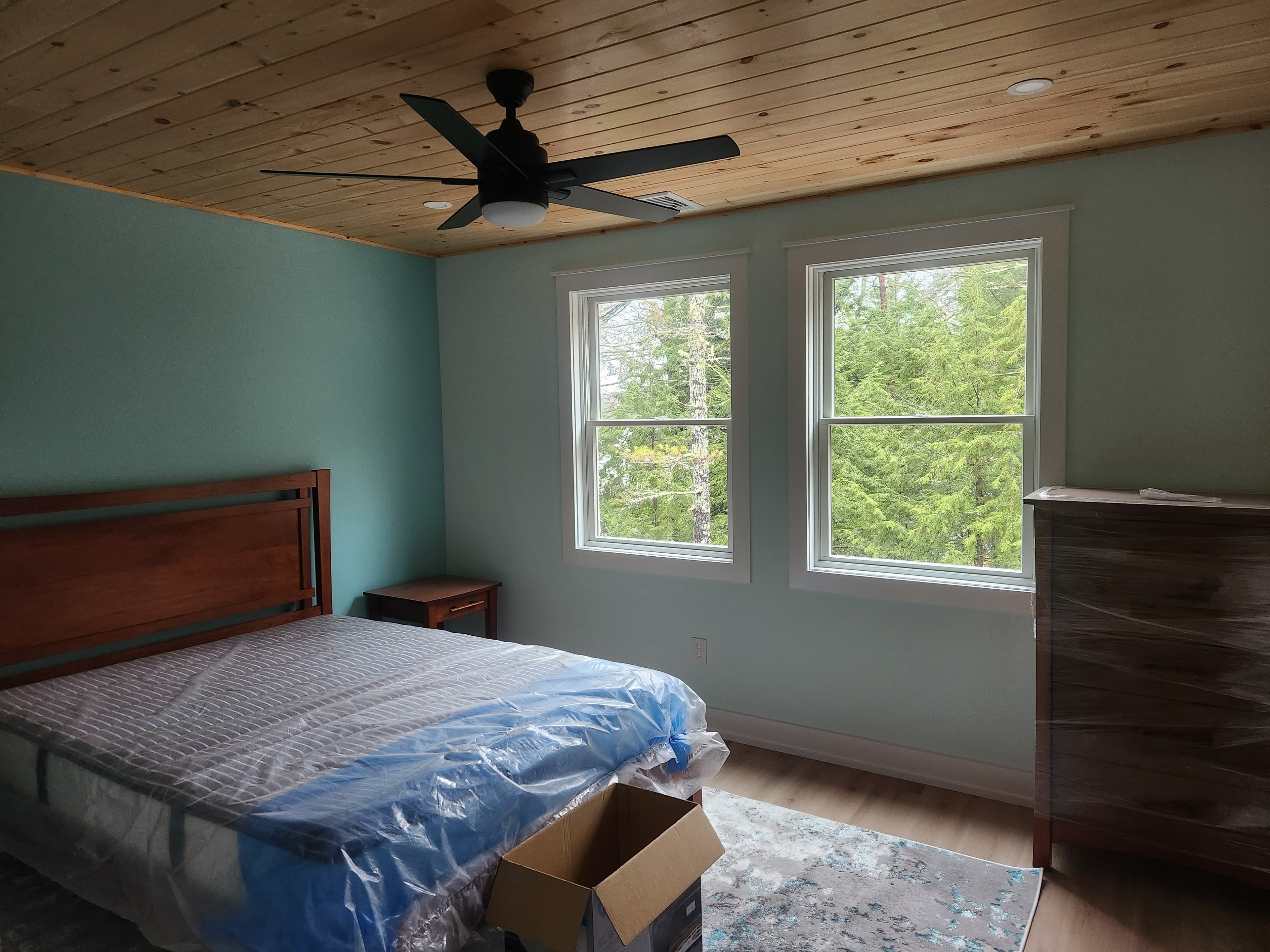 Finished bedroom with knotty pine ceiling, teal walls, cherry bed frame, and forest views