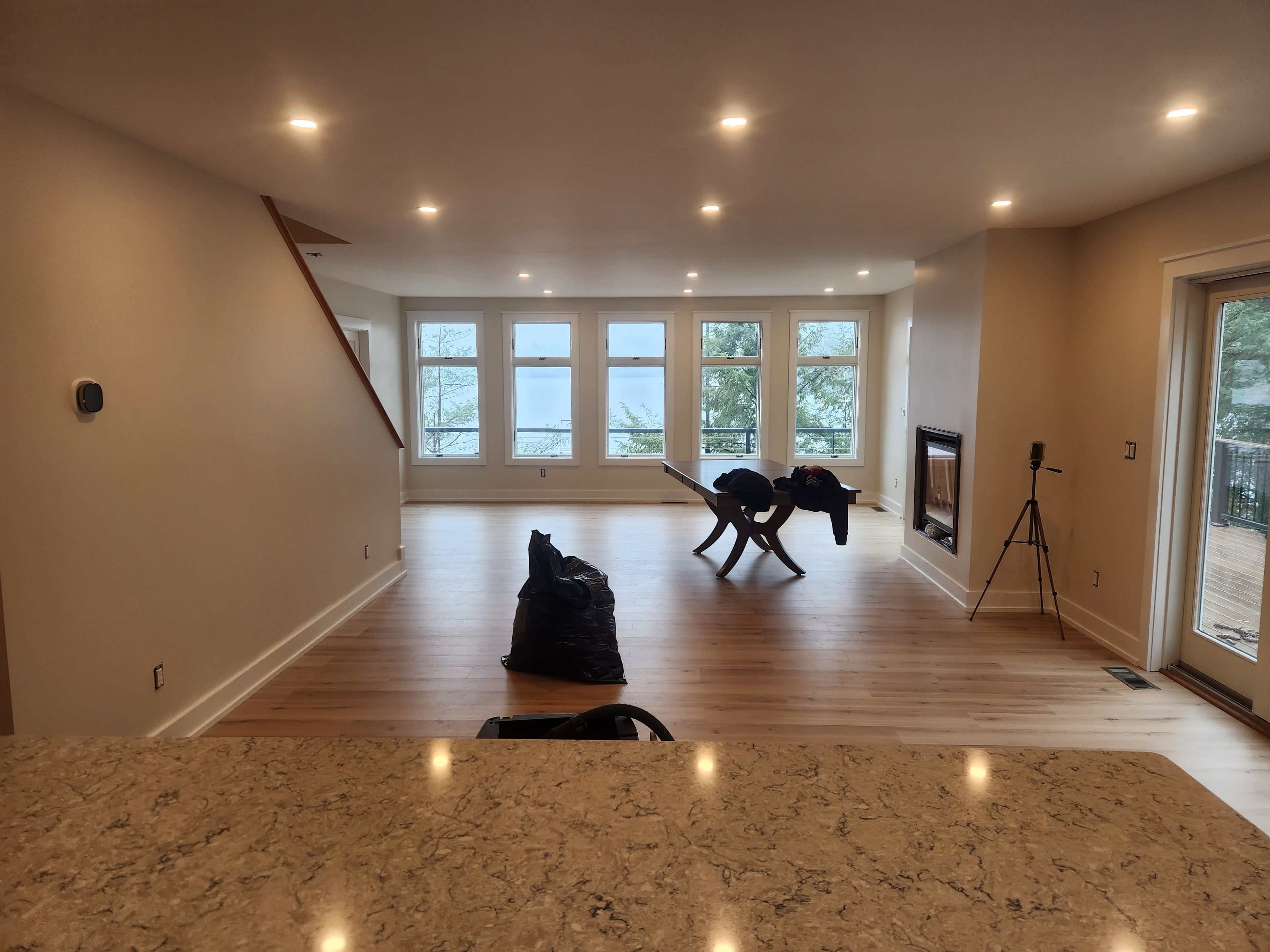 Open-plan lakeside living room near completion with granite island, hardwood floor, gas fireplace, and panoramic lake views