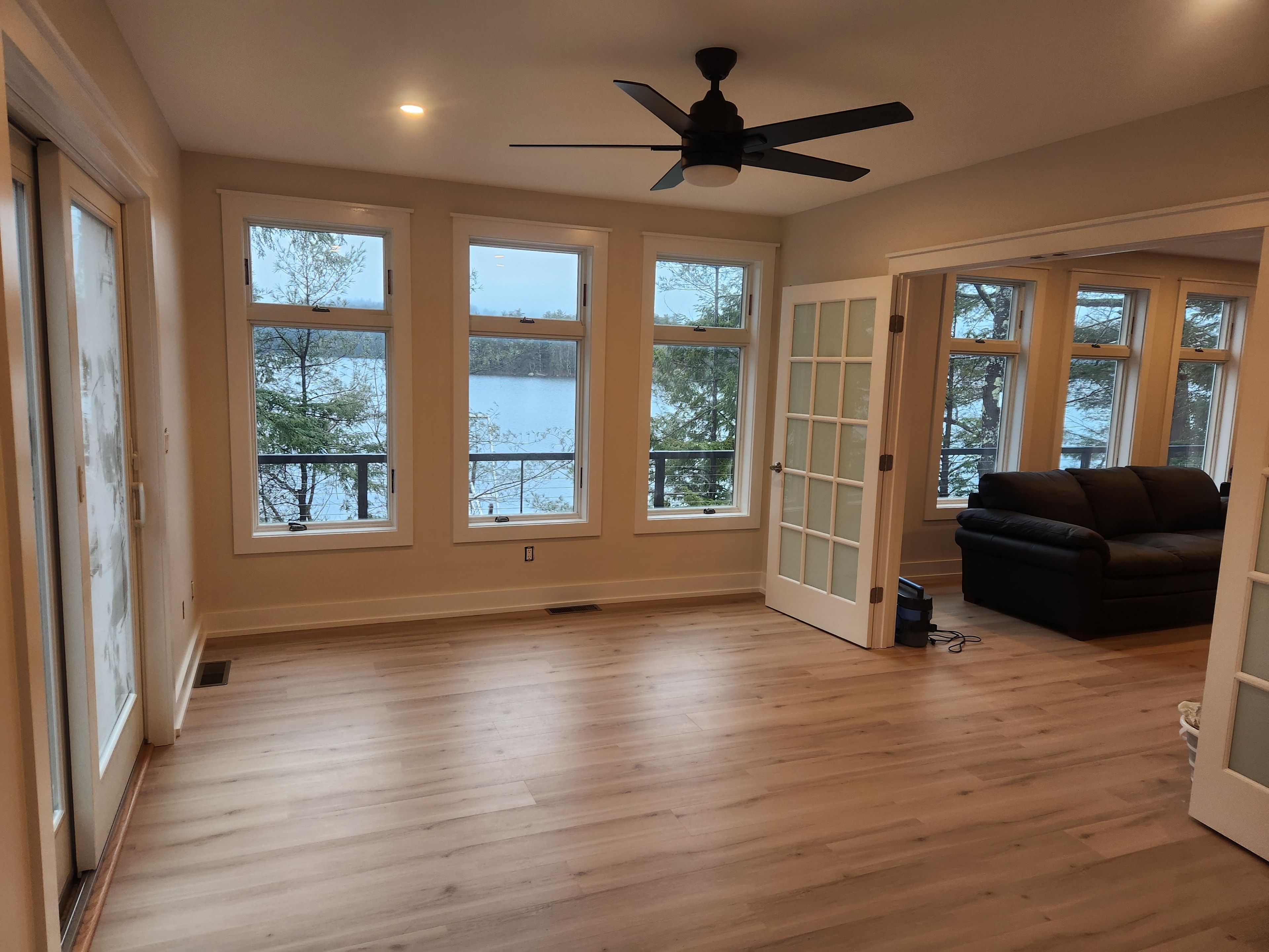 Bright sunroom with hardwood floor, ceiling fan, lake views through triple windows, and French doors to living room