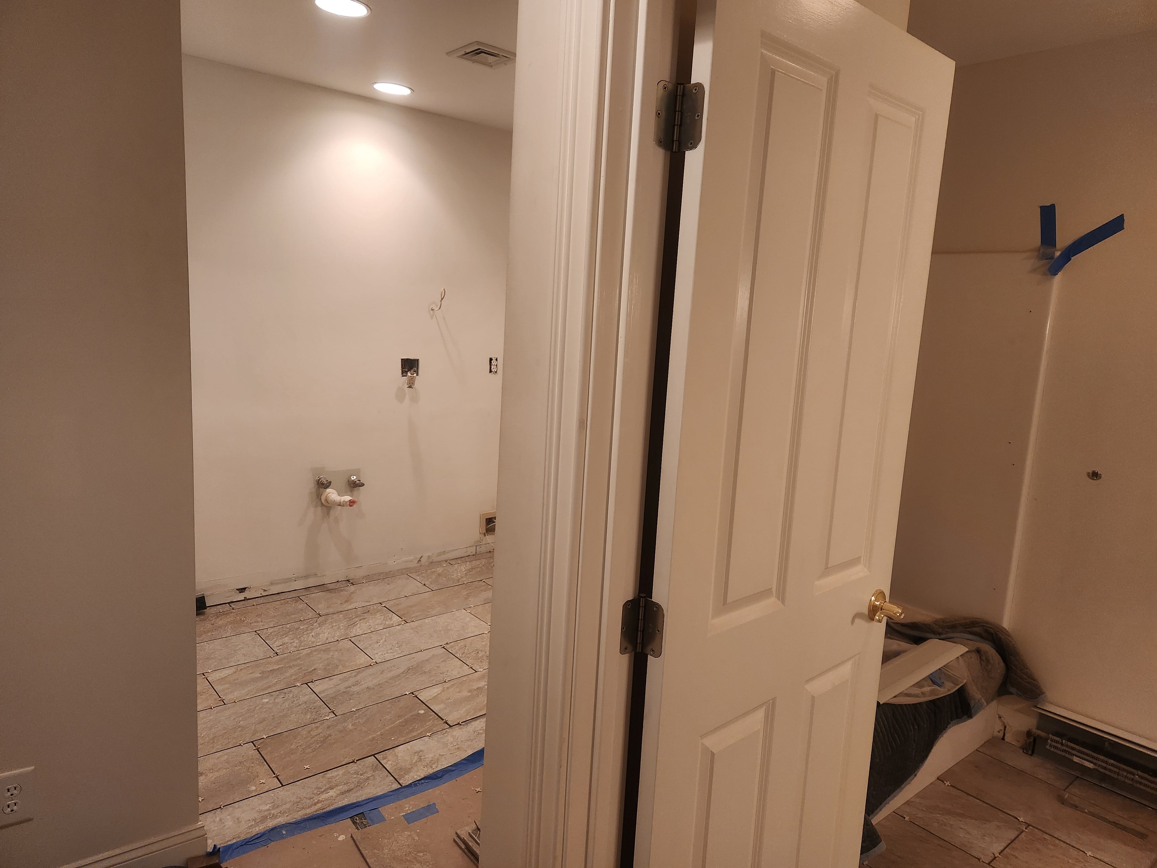 Bathroom rough-in with stone tile floor installed, plumbing stubbed out, and white panel door