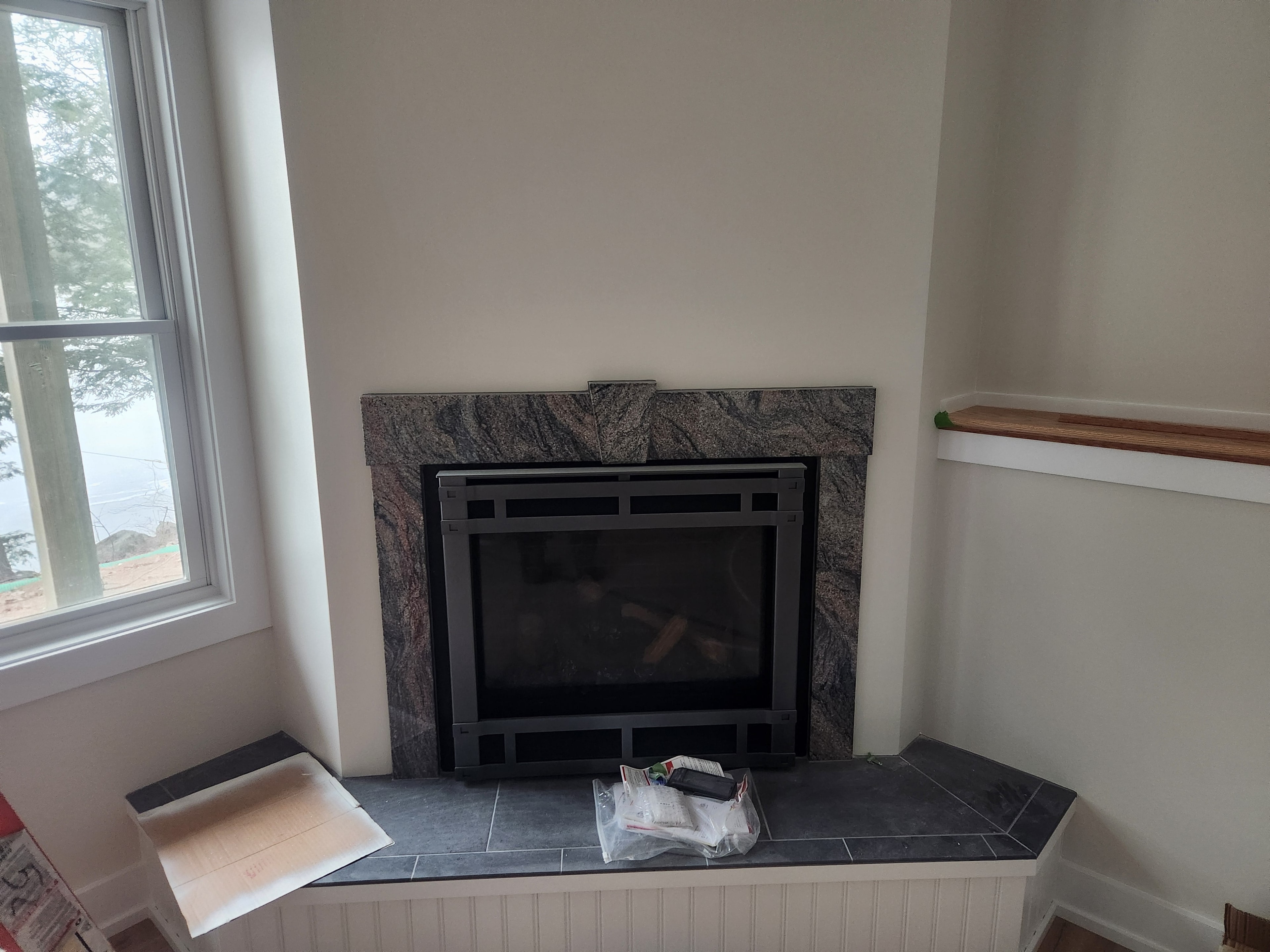 New construction granite fireplace surround with slate tile hearth, craftsman-style insert, and lake view window