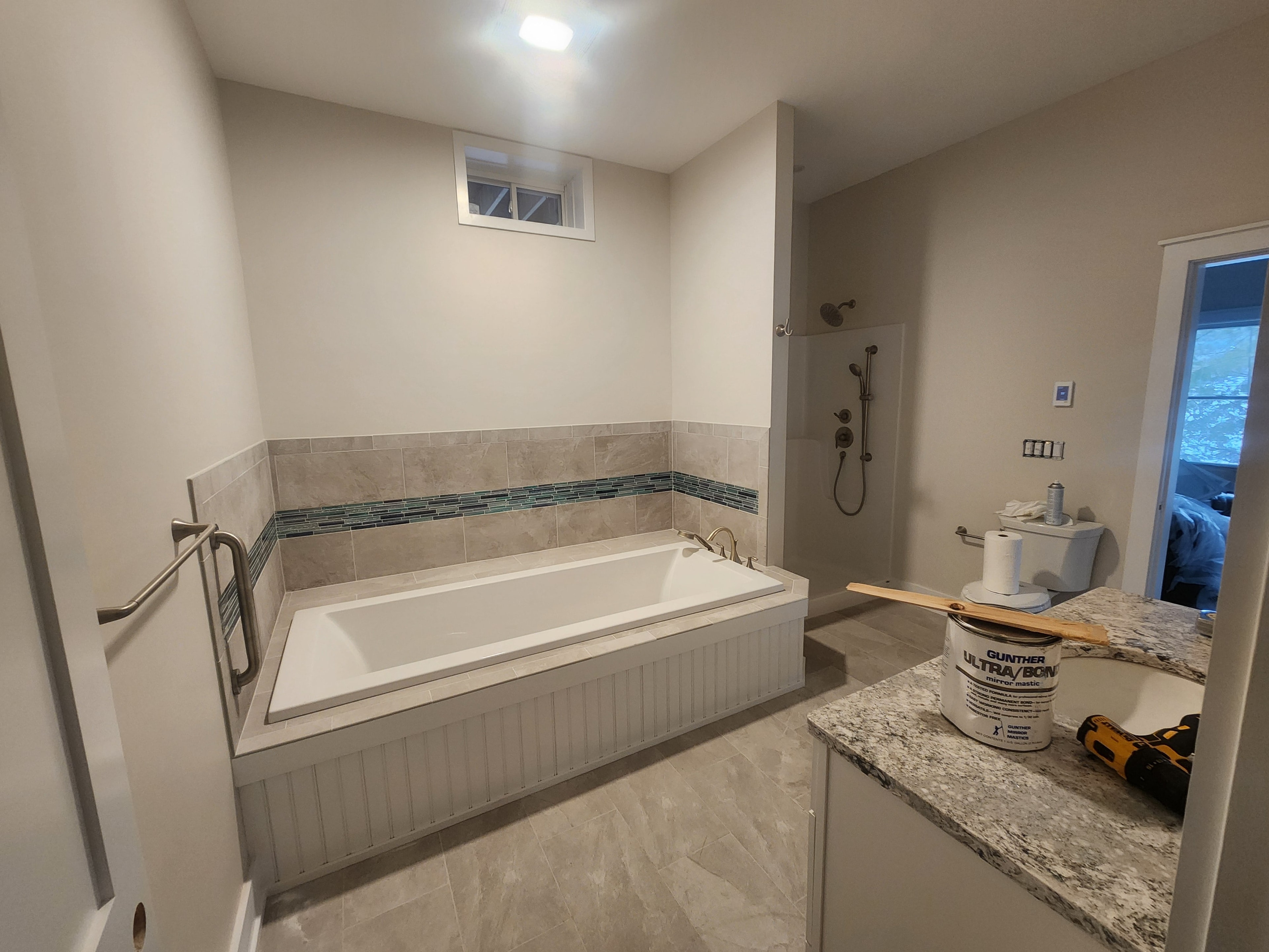 New construction master bathroom near completion with tiled soaking tub surround, glass mosaic accent strip, walk-in shower, and granite vanity