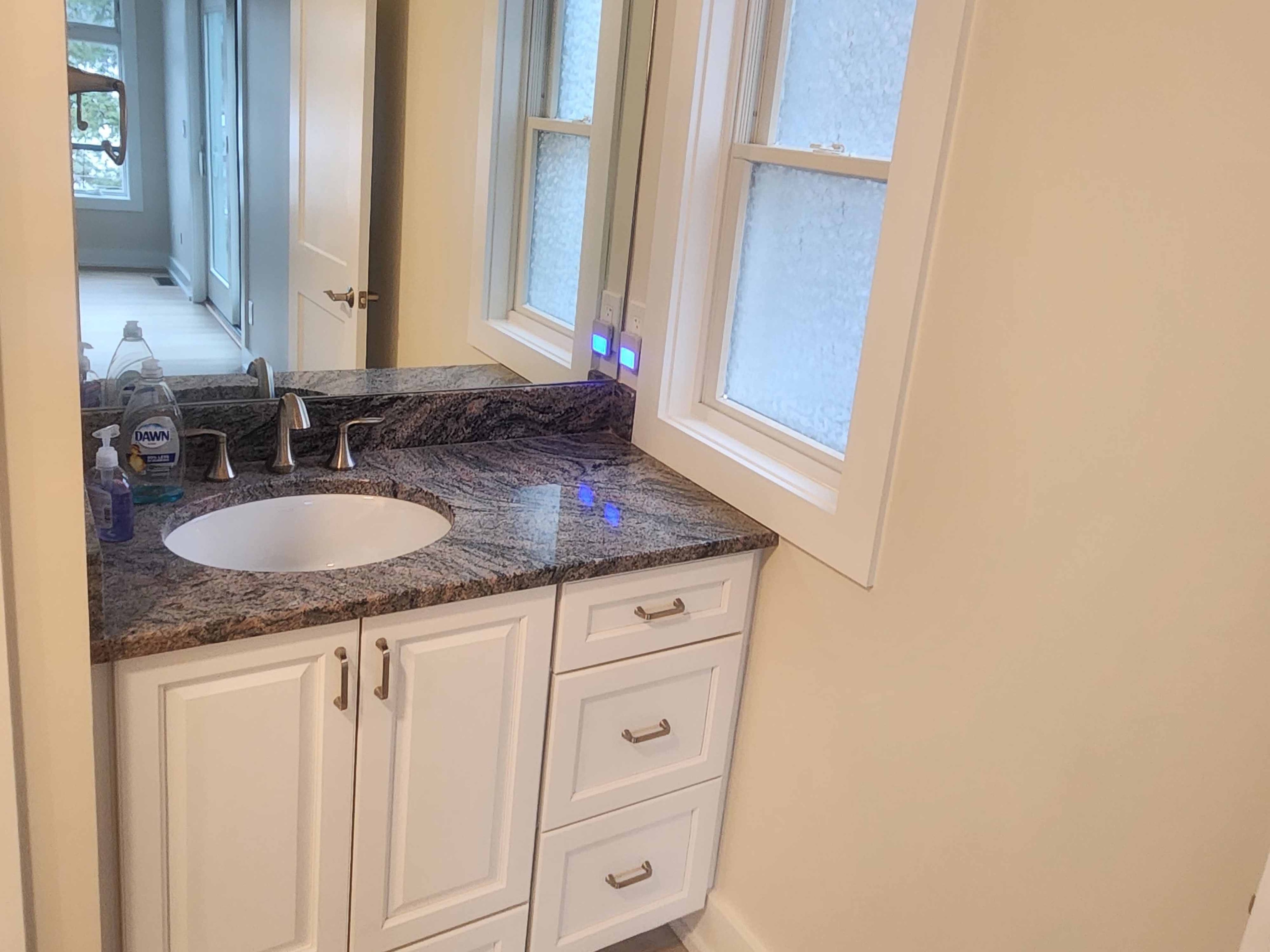 White shaker vanity with dramatic dark swirling granite countertop, undermount sink, brushed nickel faucet, and frosted privacy windows