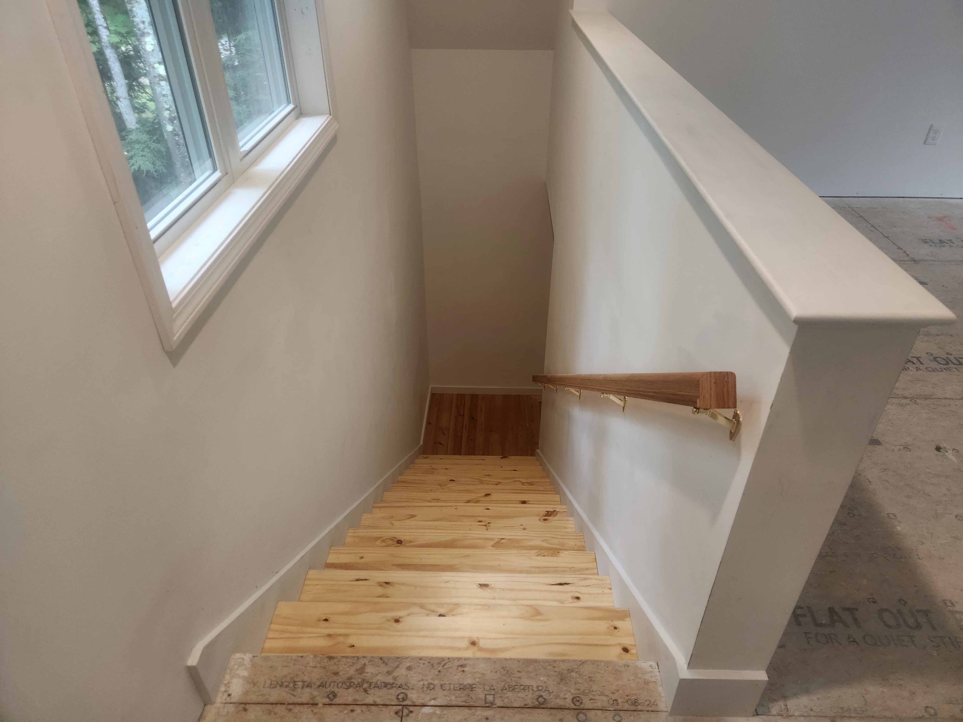 New construction pine staircase with wood handrail looking down from upper landing with wooded window view and Advantech subfloor