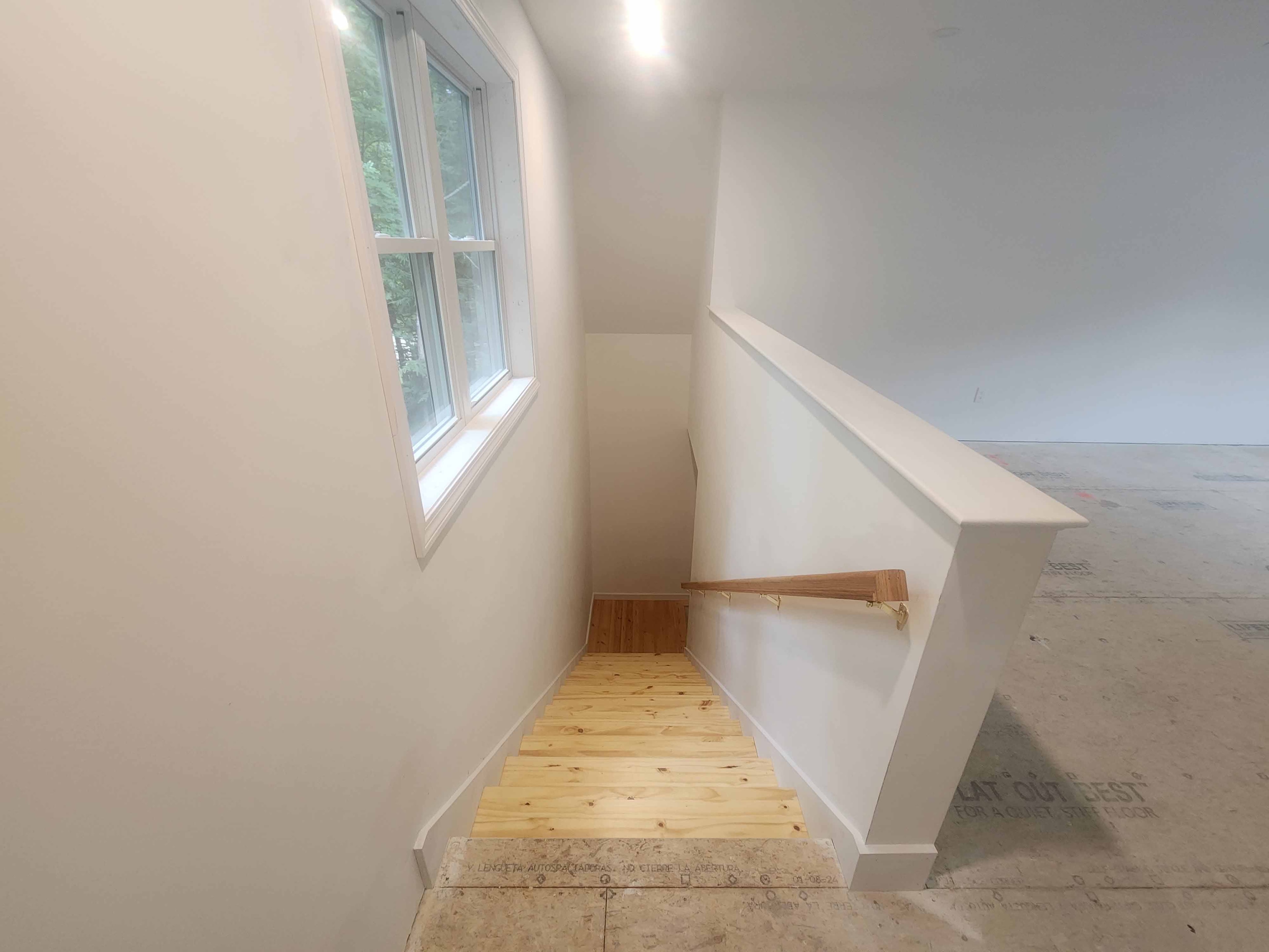 New construction staircase with pine treads and wood handrail viewed from upper landing with large window and Advantech subfloor