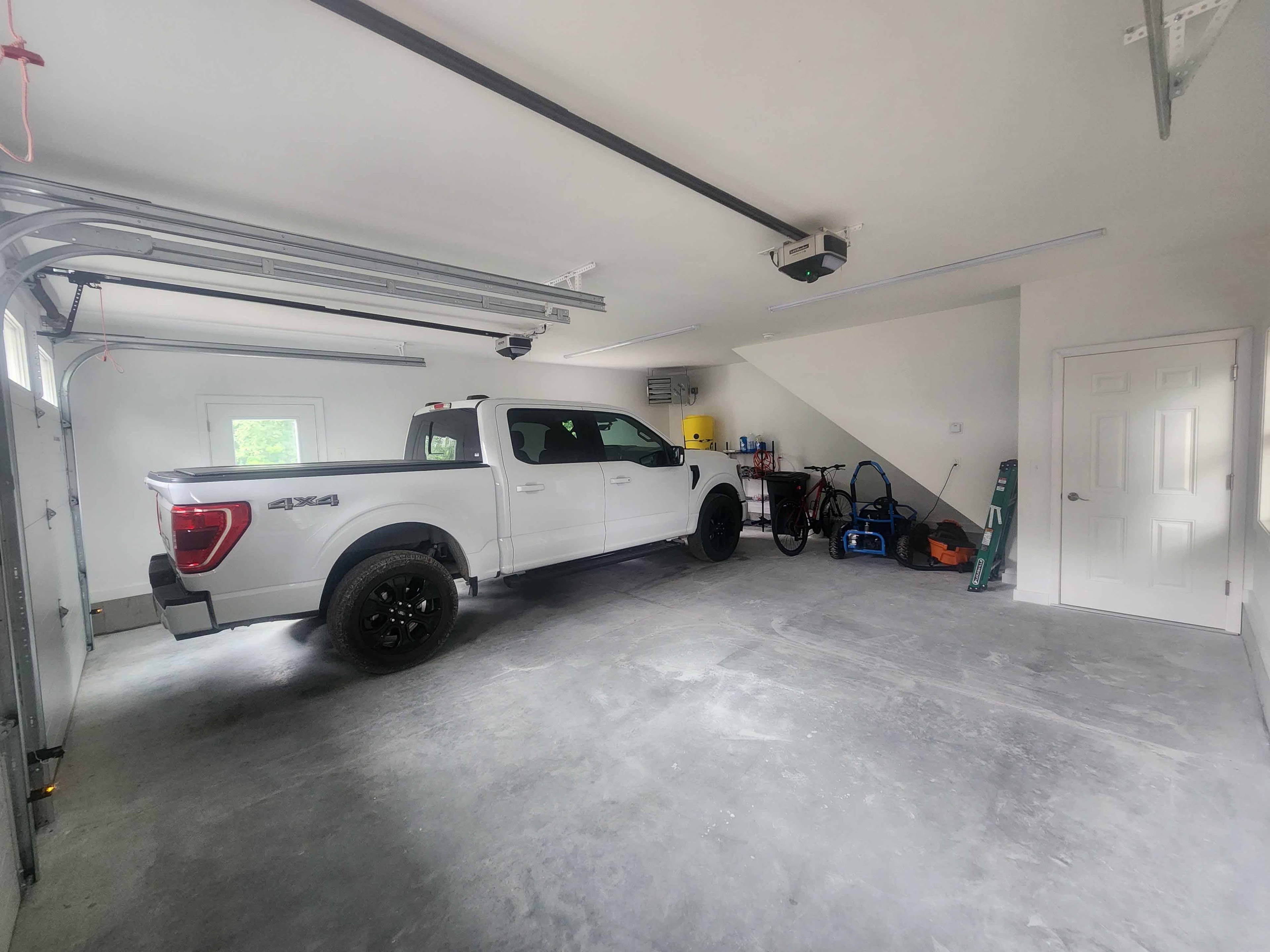 Finished two-car garage with smooth concrete floor, white walls, automatic opener, and white Ford F-150 4x4 parked inside